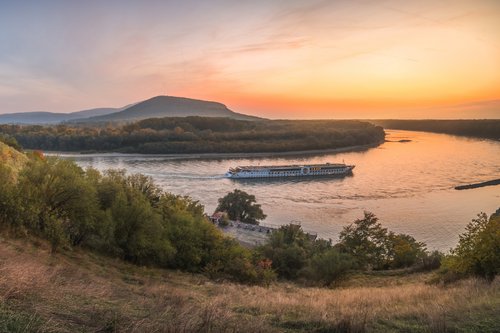 Panoramablick vom Ufer auf die Donau bei Bratislava während des Sonnenuntergangs. Ein Flussschiff fährt vorbei.