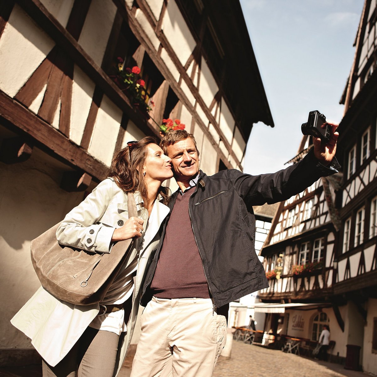 Ein Paar ist auf Entdeckungstour durch Straßburg. Sie machen ein Selfie in einer historischen Straße mit vielen Fachwerkhäusern.