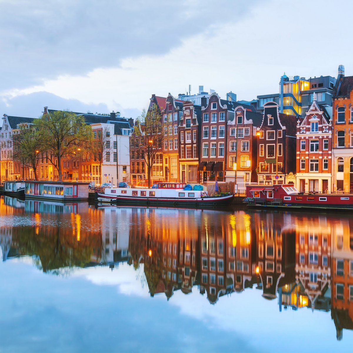 Blick auf Amsterdams Grachten mit historischen Gebäuden und Booten auf dem Wasser, während der Abenddämmerung.