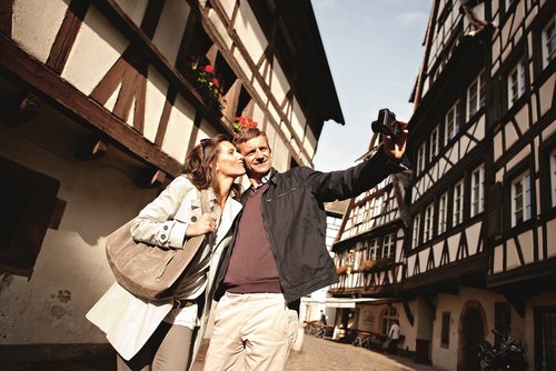 Ein Paar ist auf Entdeckungstour durch Straßburg. Sie machen ein Selfie in einer historischen Straße mit vielen Fachwerkhäusern.